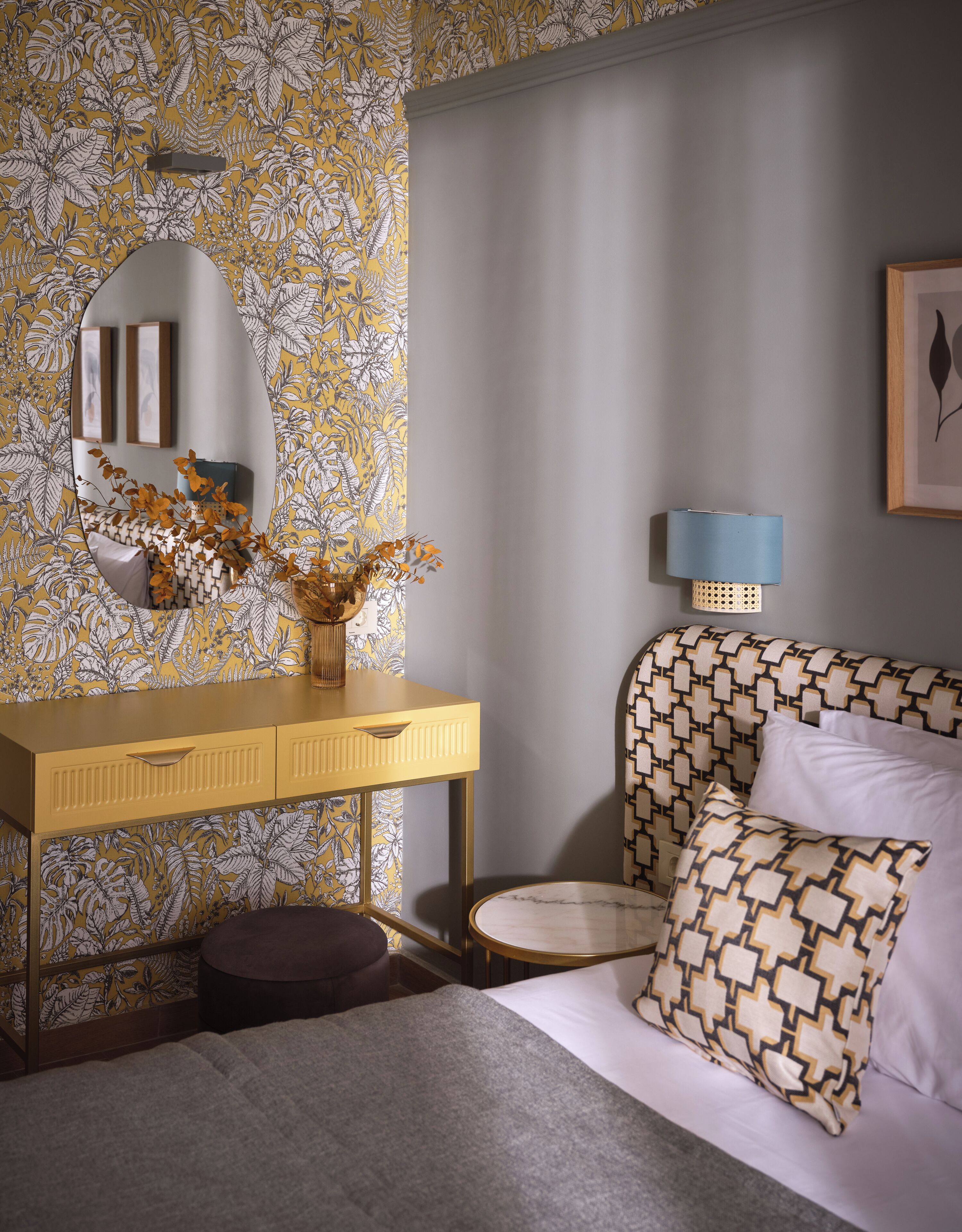 Un dormitorio con cama, mesita de noche, espejo, lámpara y papel tapiz con estampado floral.
