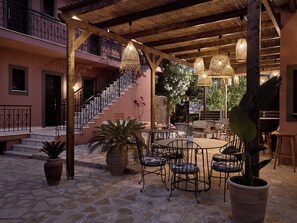 An outdoor patio area with stone flooring, a round table, and metal chairs. - Anemelia Retreat (Zakynthos)