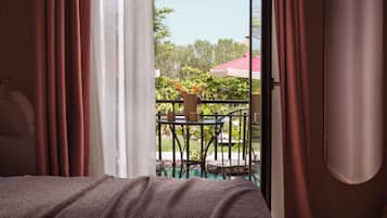 A room with a bed, curtains, and a view of an outdoor area with a table, chairs, and a red umbrella.