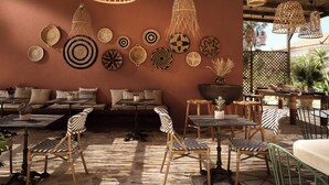 A cozy outdoor seating area with wicker furniture, a variety of woven wall decorations, and hanging light fixtures. - Anemelia Retreat (Zakynthos)