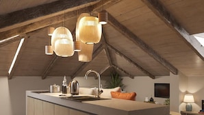 A modern kitchen with a large island, pendant lighting, and a high ceiling with exposed beams. - Anemelia Retreat (Zakynthos)