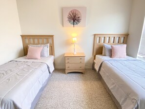 A bedroom with two beds, a nightstand with a lamp, and a wall art piece.