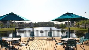 Une terrasse en bois avec des sièges et des parasols, donnant sur un lac.