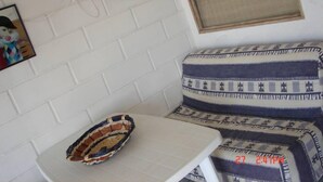 Un coin de pièce avec un mur en briques blanches, une petite table sur laquelle repose un panier en osier, un coussin à motifs et un cadre photo.