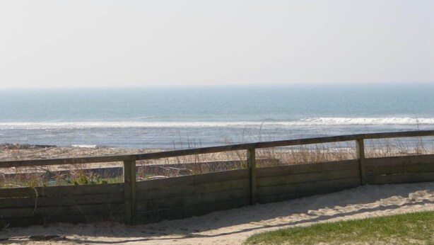 Une plage avec une clôture en bois et une zone sablonne au premier plan.