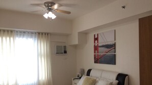 Une chambre à coucher avec un lit, un ventilateur de plafond, une fenêtre avec des rideaux, un appareil de climatisation et un tableau au mur.