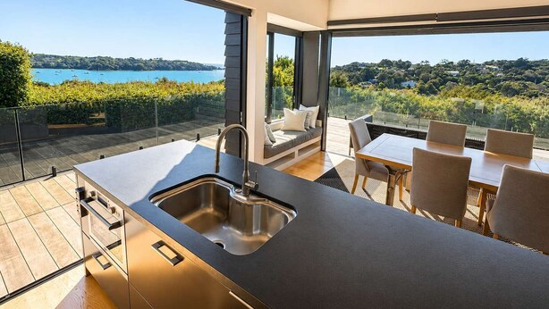 A modern kitchen with a large island, a dining area with chairs, and a view of the sea.