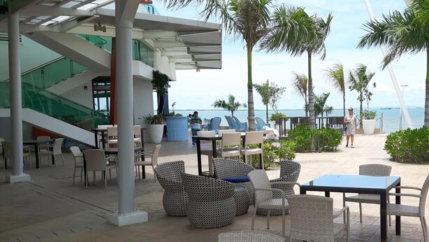 An outdoor seating area with wicker furniture and a glass table, overlooking a beach and palm trees. - Lux. 2 BR Condo Seaside Close to SM Seaside Megamall-Huge pools (Cebu City)