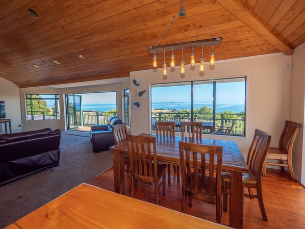 Uma sala de estar ampla com uma mesa de jantar de madeira e cadeiras, um sofá de couro e uma varanda com vista para o oceano.