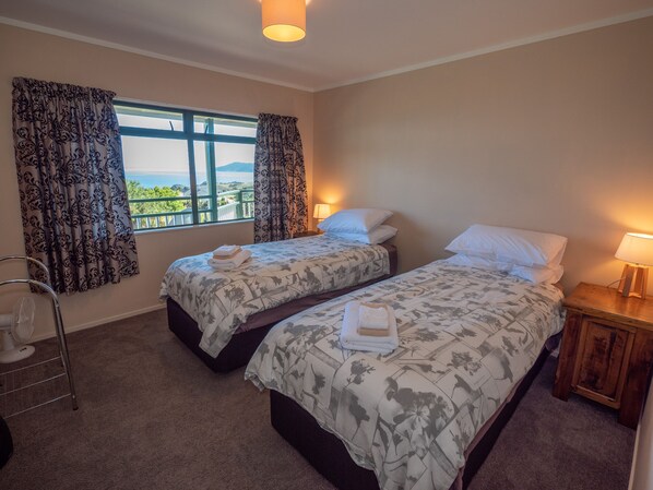 A hotel room with two beds, a window with curtains, a bedside table with a lamp, and a chair.