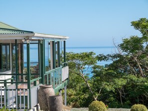 A coastal building with large windows overlooking the sea, surrounded by lush greenery.