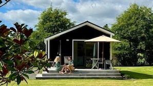 A modern house with a covered patio, a lawn, and trees in the background. - Matakana Oasis - Beauregard Cottages (Matakana)