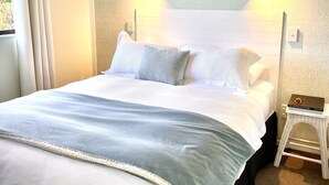 A neatly made bed with a white headboard, two bedside lamps, and a small bedside table. - Matakana Oasis - Beauregard Cottages (Matakana)
