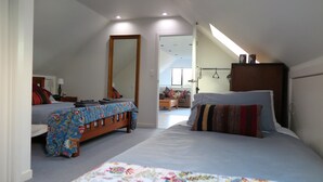 Un dormitorio con cama, mesita de noche, una silla, un espejo y una ventana.
