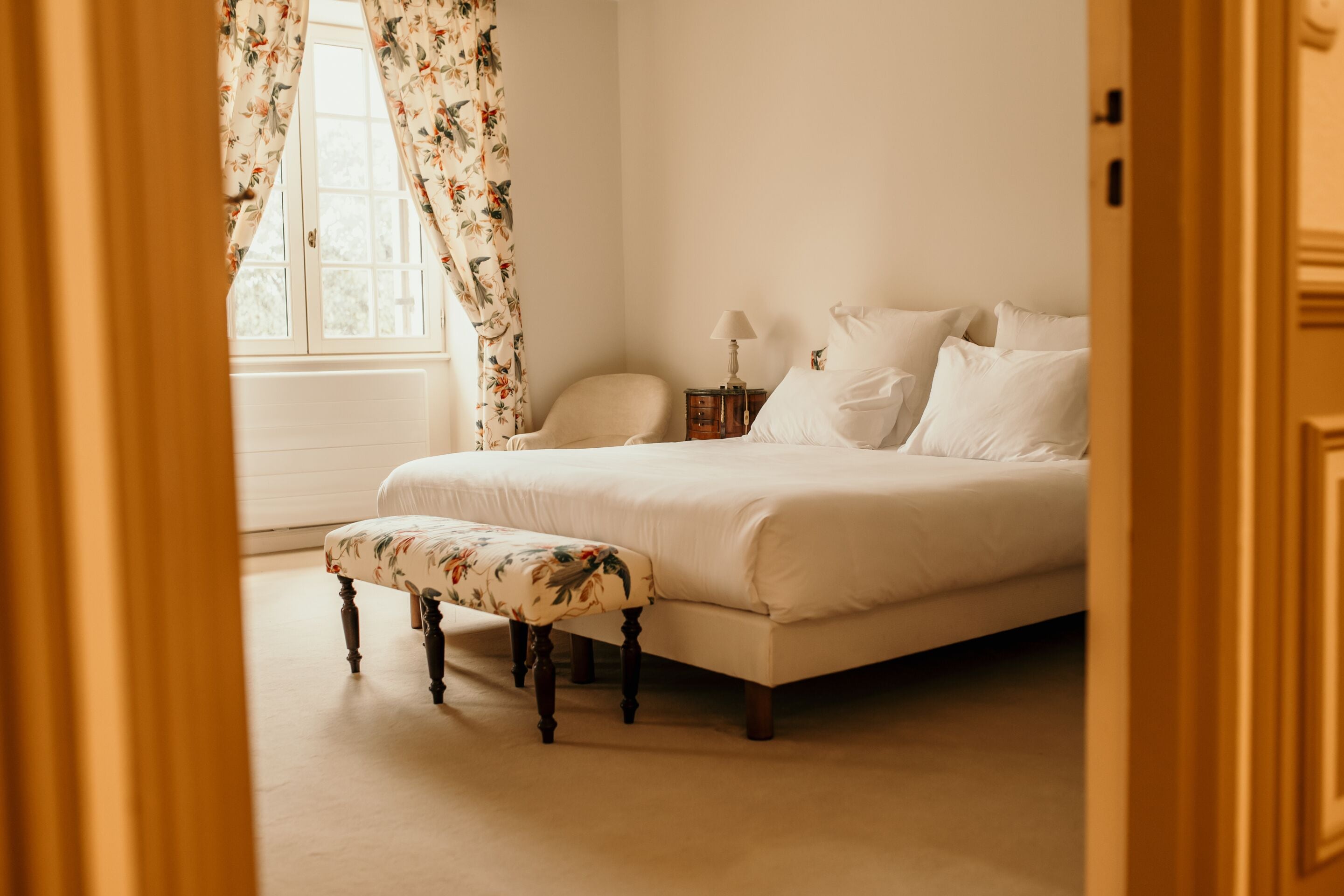A bedroom with a bed, a nightstand, a chair, and a window with curtains.