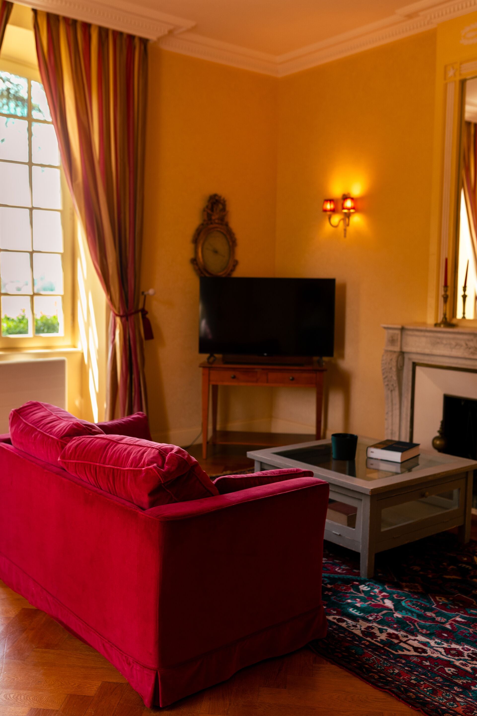 Una sala de estar con un sofá rojo, un televisor sobre un mueble, una chimenea y una alfombra estampada.