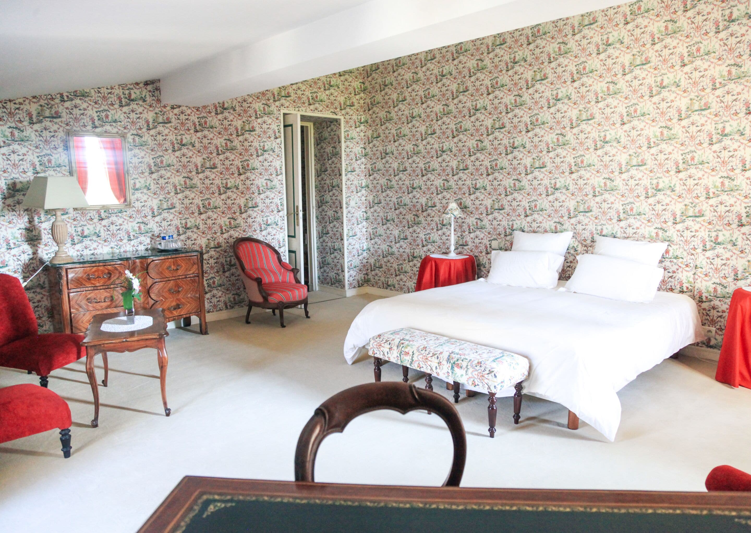 A bedroom with a bed, a chair, a small table, and a dresser.