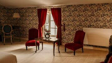 A room with patterned wallpaper, a wooden table, two red chairs, a lamp, and a window with red curtains.
