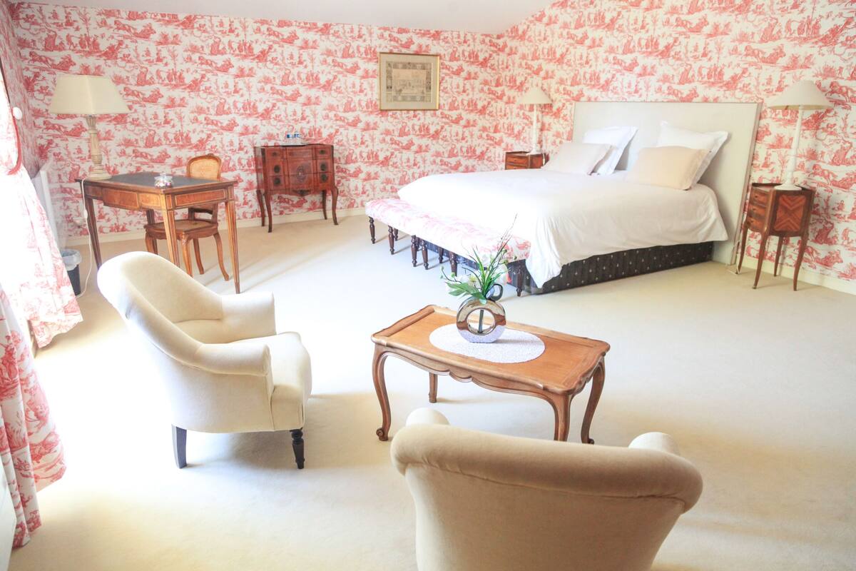 A bedroom with a large bed, two bedside tables, a desk, a chair, and a small table with a vase.