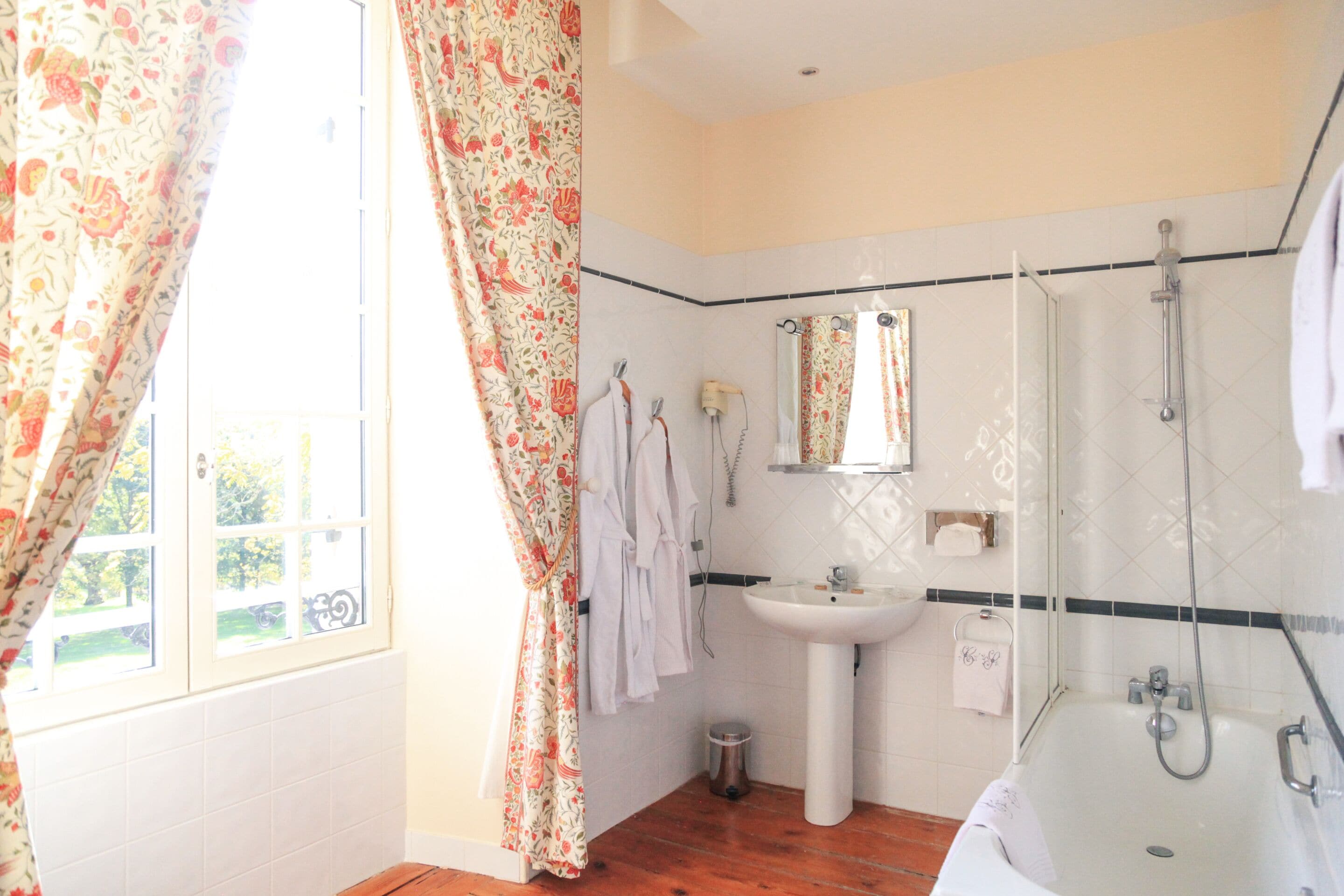 Un baño con ducha, lavamanos y ventana con cortinas.