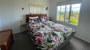 A bedroom with a bed, a nightstand, a lamp, a window with a view, and a ceiling light. - Waitarere retreat - on the dunes, panoramic sea views, minutes to the sand (Waitarere Beach)