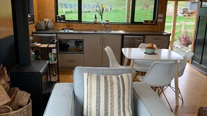 Una cucina moderna con una grande finestra, un'area pranzo con tavolo e sedie, e un divano grigio con un cuscino a righe.