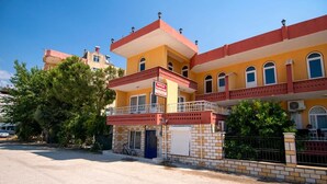 A two-story building with a red and yellow facade, a balcony, and a sign indicating a rental property. - Baykal Pansiyon (Finike)