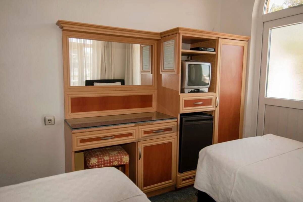 A hotel room with a wooden desk, a television, a small refrigerator, and two beds.