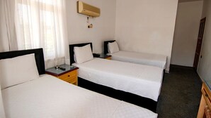 A hotel room with three single beds, a bedside table with a lamp, a wall-mounted air conditioner, and a large window with sheer curtains. - Baykal Pansiyon (Finike)