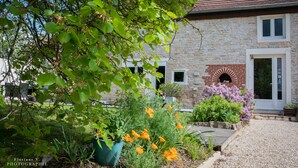A stone house with a brick fireplace, a gravel driveway, and a garden with various plants and flowers. - Aux Mésanges (Labergement-Foigney)