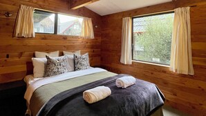 A wooden cabin room with a bed, two windows, and curtains. - Snow Chalet - Ohakune Chalet (Ohakune)