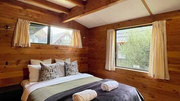 A wooden cabin room with a bed, two windows, and curtains.