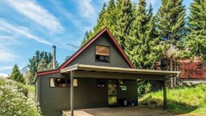 A small cabin with a red roof, a covered porch, and a door with a sign. - Snow Chalet - Ohakune Chalet (Ohakune)