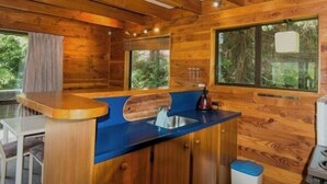 A wooden cabin interior with a kitchen area featuring a blue countertop, wooden cabinets, and a window with a view of greenery. - Snow Chalet - Ohakune Chalet (Ohakune)