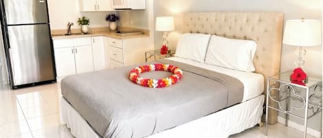 Habitación de hotel con cama, lámparas de noche, una mesita, refrigerador y zona de cocina.