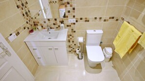 Un baño con lavamanos blanco, inodoro y bidé, paredes con azulejos y una toalla amarilla.