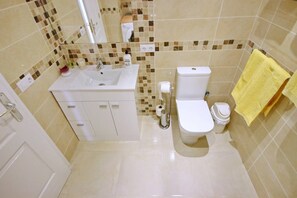 Un bagno con lavandino, water e bidet bianchi, pareti piastrellate e un asciugamano giallo.