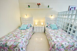 A bedroom with two beds, a nightstand, a dresser, and a decorative wall with glass panels.