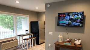 A modern kitchen with a refrigerator, a dining area with a table and benches, a wall-mounted TV displaying Netflix, and a Wi-Fi sign.