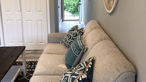 A living room with a beige sectional sofa, patterned pillows, a wooden coffee table, and a decorative wall clock.