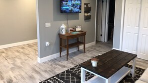 A modern living room with a flat-screen TV mounted on the wall, a wooden coffee table, and a patterned rug.