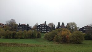 Une rangée d’immeubles modernes à plusieurs étages, dotés de balcons, et entourés de champs verdoyants et d’arbres.