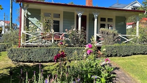 A house with a porch, a chimney, and a garden with various plants and flowers.