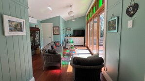 A cozy living room with a wicker sofa, a television, and a large window with green-tinted glass.