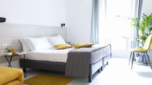 Un dormitorio moderno con una cama, mesitas de noche, una silla y una planta.