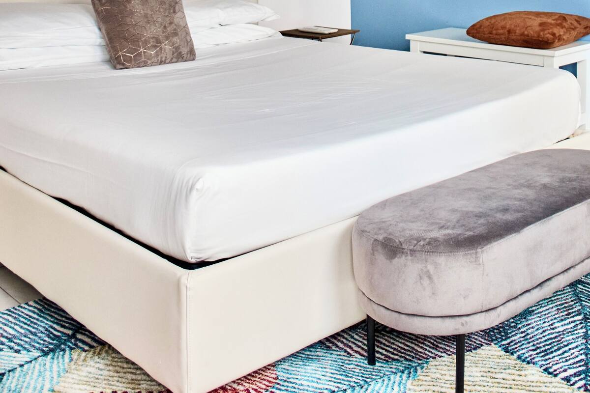 Ein Schlafzimmer mit einem weißen Bett, einer grauen Bank, einer Holzbalkendecke und einer blauen Wand.