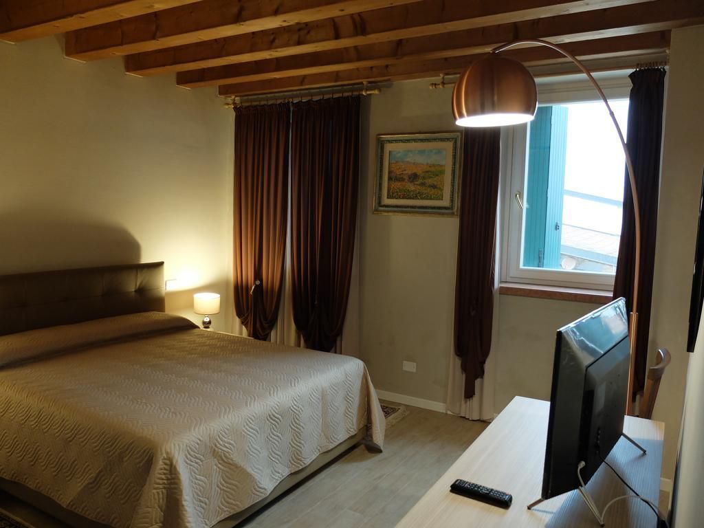 A bedroom with a bed, a desk with a computer, a lamp, and a window with curtains.