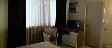 Un dormitorio con cama, escritorio, televisor y puerta.