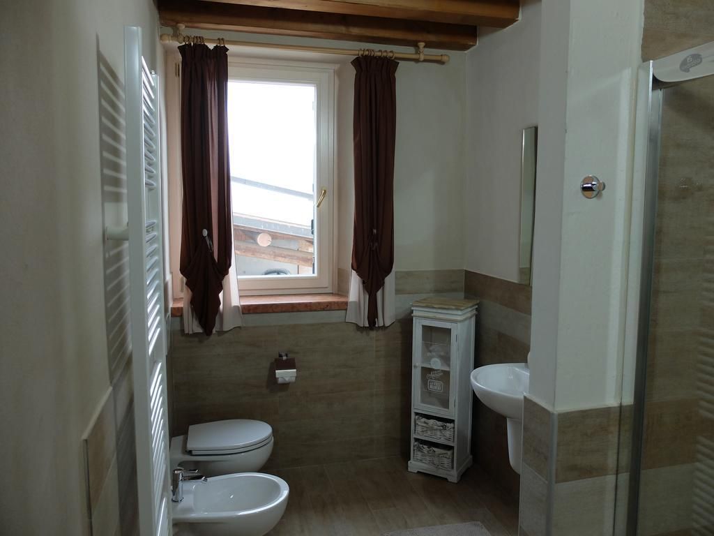 A compact bathroom with a toilet, bidet, and sink. There is a window with curtains, a small cabinet, and a mirror.