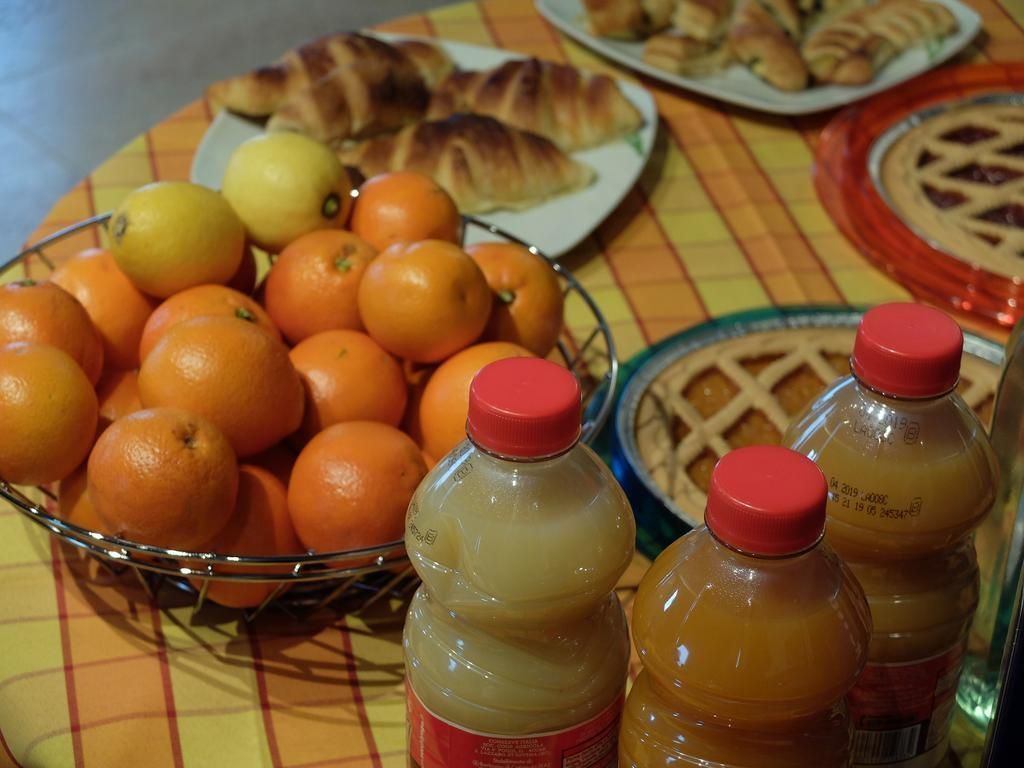 A table with a fruit bowl containing oranges and lemons, and three bottles of juice.